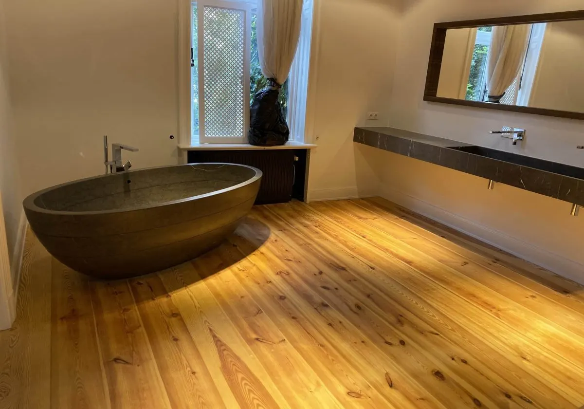 Fertiges Badezimmer mit freistehender Steinwanne, langem Doppelwaschtisch aus dunklem Naturstein und breitem Dielenboden